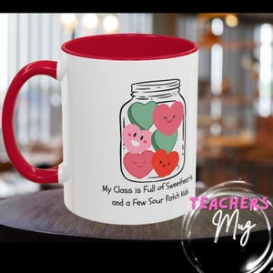 Puede incluir: Taza de cerámica blanca con interior y asa rojos. La taza presenta una ilustración de un tarro lleno de caramelos en forma de corazón en rosa y verde. El texto en la taza dice: "My Class is Full of Sweethearts and a Few Sour Patch Kids".