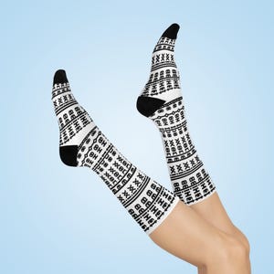May include: White socks with black accents and a repeating text pattern. The socks have black toes and heels. The text on the socks reads "8H the xer xxi adiust". The socks are on a light blue background.