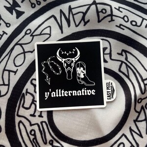 May include: Black and white sticker with a bull skull, a cowboy boot, and a barbed wire lasso. The text "y'allternative" is below the image.