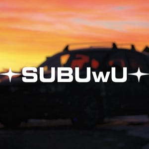 以下が含まれることがあります： 後部窓に白い文字で「SUBUWU」と書かれた黒い車。車は夕日の前に駐車されている。