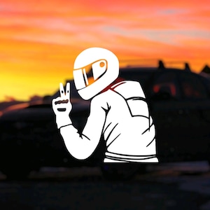 Puede incluir: Una silueta blanca de una persona con casco y haciendo un signo de paz, con un coche negro en el fondo. La imagen está sobre un cielo de puesta de sol.