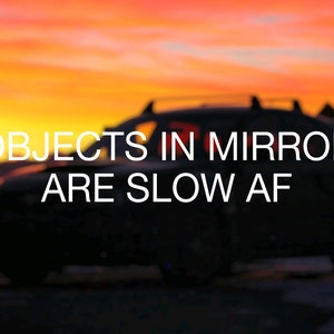 May include: A black car with a spoiler and the text "OBJECTS IN MIRROR ARE SLOW AF" on the back window. The car is parked in front of a sunset sky.