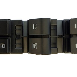 May include: Black plastic car window control panel with four buttons. The top left button has a symbol for a window lock, the bottom left button has a symbol for a window lock, the top right button has the word "AUTO" and the bottom right button has the word "AUTO".