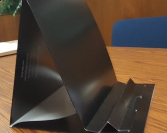 May include: Black cardboard phone stand with a triangular base and a fold-out stand. The stand is designed to hold a phone upright.