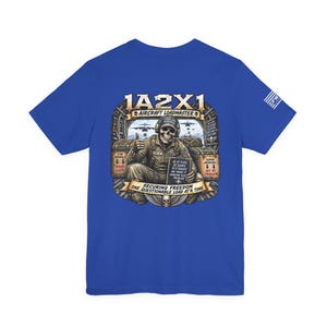 May include: A royal blue short-sleeve t-shirt featuring a graphic on the back of a skeleton dressed as an aircraft loadmaster. The design includes the text 1A2X1 AIRCRAFT LOADMASTER, SECURING FREEDOM ONE QUESTIONABLE LOAD AT A TIME, and IF IT FITS IT SHIPS.