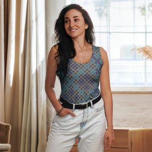 Peut inclure: Une femme portant un débardeur sans manches avec un motif géométrique dans les tons bleus, verts et rouges. Le débardeur a un col rond et une silhouette ajustée. Elle porte un jean bleu et une ceinture marron.