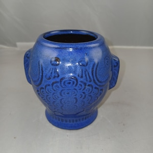 May include: A blue ceramic vase with a textured surface and a dark interior. The vase features decorative patterns and two small handles on either side. The vase is approximately 5 inches tall.