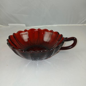 May include: A deep red glass bowl with a scalloped rim and a single handle. The bowl is made of clear glass with a reddish tint.