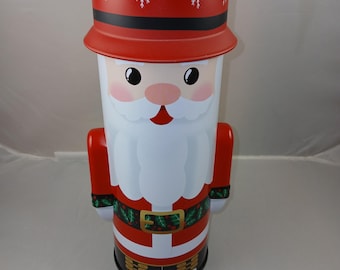 May include: A red and white Santa Claus Christmas tin with a black belt and holly design. The tin has a red hat with white snowflakes.
