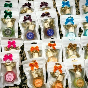 May include: Assortment of small glass bottles with wooden stoppers and colourful ribbons, packaged in clear plastic bags. The bottles are filled with a clear liquid and have a decorative label.