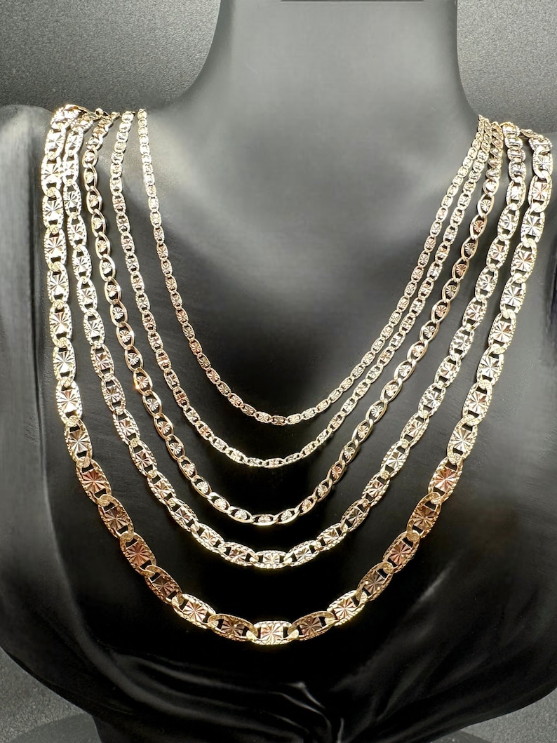 May include: Five gold chains of different lengths and widths, all with a textured, diamond-cut design. The chains are displayed on a black velvet mannequin.
