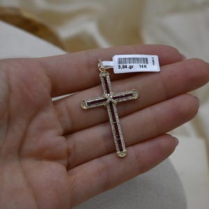 Puede incluir: Un colgante de cruz de oro con piedras rojas y blancas. El colgante pesa 3,04 gramos y es de oro de 14 quilates.