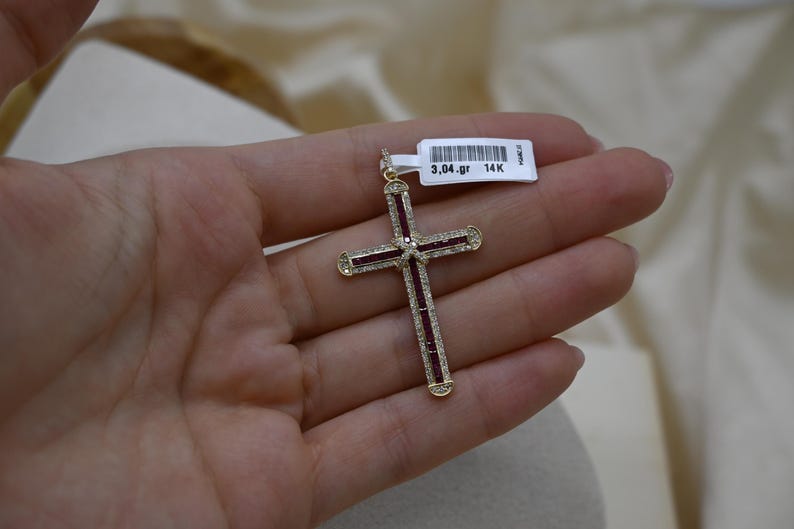 Puede incluir: Un colgante de cruz de oro con piedras rojas y blancas. El colgante pesa 3,04 gramos y es de oro de 14 quilates.