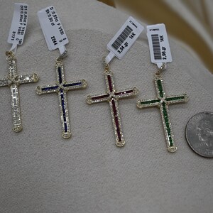 Puede incluir: Cuatro colgantes de cruz de oro con piedras preciosas de diferentes colores. Las cruces est&aacute;n engastadas con peque&ntilde;os diamantes y tienen un acabado pulido. Las piedras preciosas son azules, rojas, verdes y transparentes. Los colgantes se muestran sobre una superficie blanca con etiquetas de precio.
