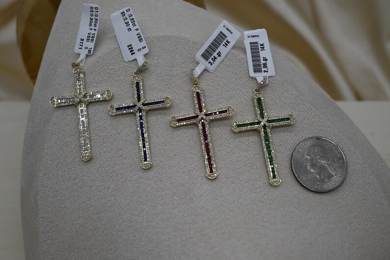 Puede incluir: Cuatro colgantes de cruz de oro con piedras preciosas de diferentes colores. Las cruces est&aacute;n engastadas con peque&ntilde;os diamantes y tienen un acabado pulido. Las piedras preciosas son azules, rojas, verdes y transparentes. Los colgantes se muestran sobre una superficie blanca con etiquetas de precio.