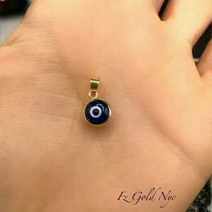 Puede incluir: Un colgante de oro con un amuleto de ojo turco azul. El amuleto tiene un c&iacute;rculo blanco en el centro.