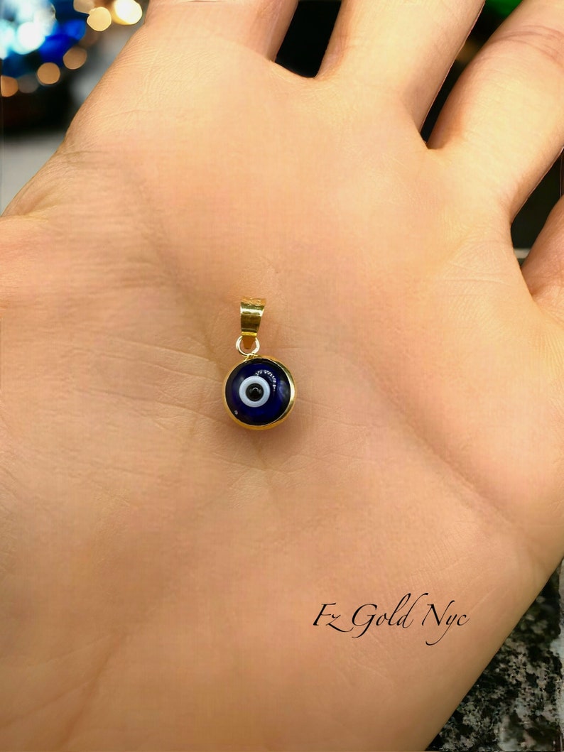 Puede incluir: Un colgante de oro con un amuleto de ojo turco azul. El amuleto tiene un c&iacute;rculo blanco en el centro.