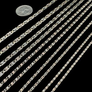 May include: A set of eight silver chains with different styles and sizes. The chains are laid out in a diagonal pattern on a black background. A quarter is included for scale.