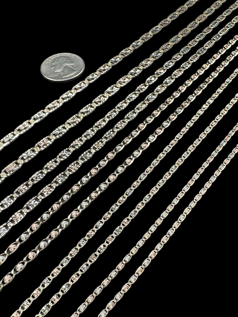 May include: A set of eight silver chains with different styles and sizes. The chains are laid out in a diagonal pattern on a black background. A quarter is included for scale.