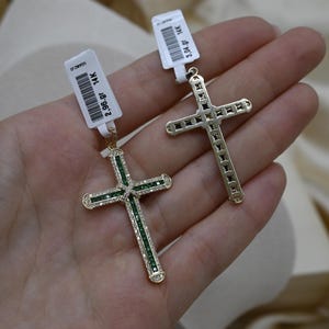 Puede incluir: Dos colgantes de cruz de oro con piedras preciosas verdes. La cruz de la izquierda es m&aacute;s peque&ntilde;a y est&aacute; adornada con piedras preciosas m&aacute;s peque&ntilde;as. La cruz de la derecha es m&aacute;s grande y tiene piedras preciosas m&aacute;s grandes.