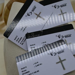 Puede incluir: Cuatro tarjetas blancas con texto negro y un colgante de cruz de oro en cada tarjeta. Las tarjetas tienen el texto "DIAMOND" y "BZ GOLD NEW YORK". Las tarjetas tambi&eacute;n tienen informaci&oacute;n sobre el oro y las piedras utilizadas en el colgante, incluyendo el quilate, el peso y el tama&ntilde;o de las piedras.