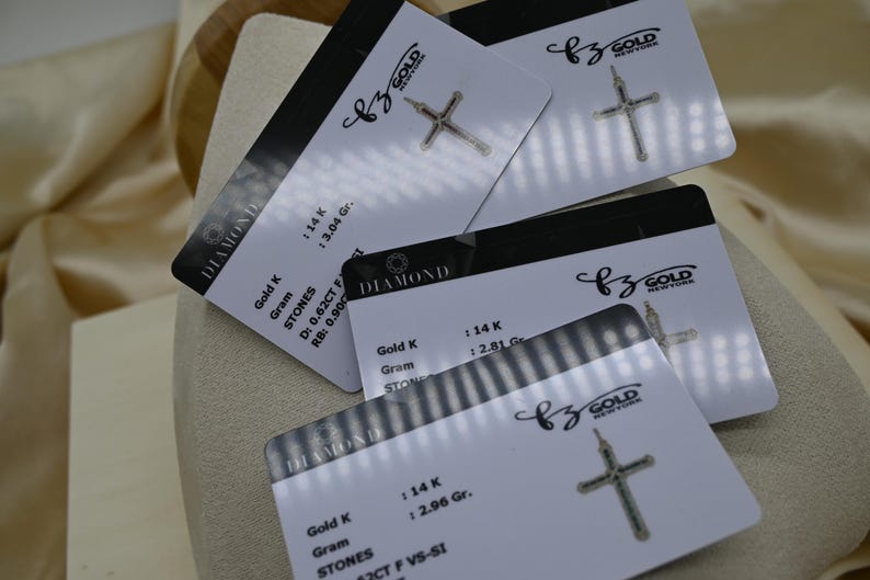 Puede incluir: Cuatro tarjetas blancas con texto negro y un colgante de cruz de oro en cada tarjeta. Las tarjetas tienen el texto "DIAMOND" y "BZ GOLD NEW YORK". Las tarjetas tambi&eacute;n tienen informaci&oacute;n sobre el oro y las piedras utilizadas en el colgante, incluyendo el quilate, el peso y el tama&ntilde;o de las piedras.