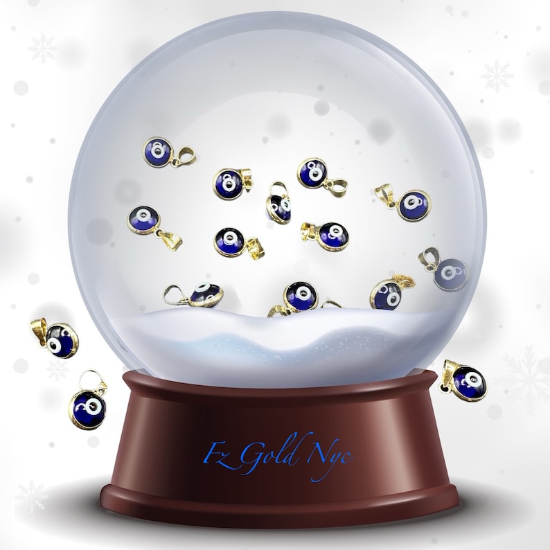 Puede incluir: Un globo de nieve con una base marr&oacute;n y una c&uacute;pula de vidrio transparente. Dentro del globo, hay muchos peque&ntilde;os amuletos de ojo turco azules y dorados. La base del globo de nieve tiene el texto "F2 Gold NYC" escrito en &eacute;l.