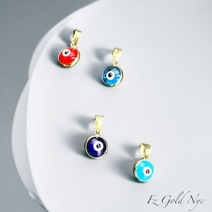 Puede incluir: Cuatro colgantes de oro con amuletos de ojo turco azul y blanco. Un colgante tiene un amuleto de ojo turco rojo.