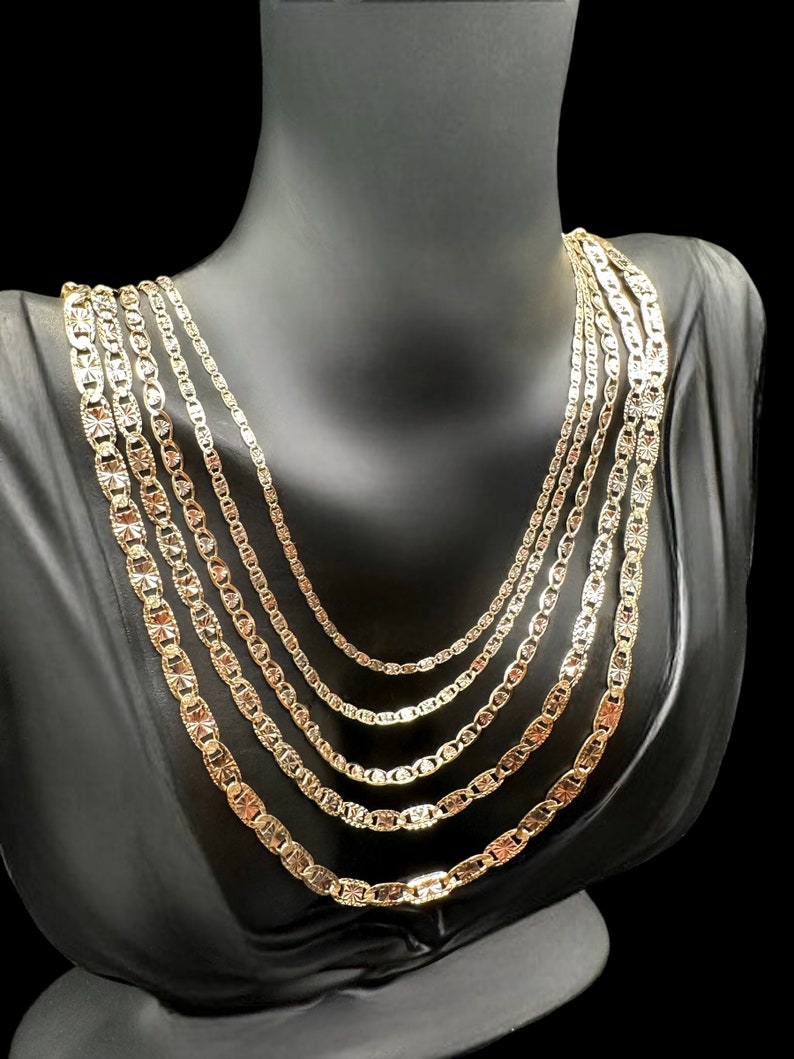 May include: A set of five gold chains of varying lengths and widths, all featuring a textured, patterned design. The chains are displayed on a black mannequin bust.