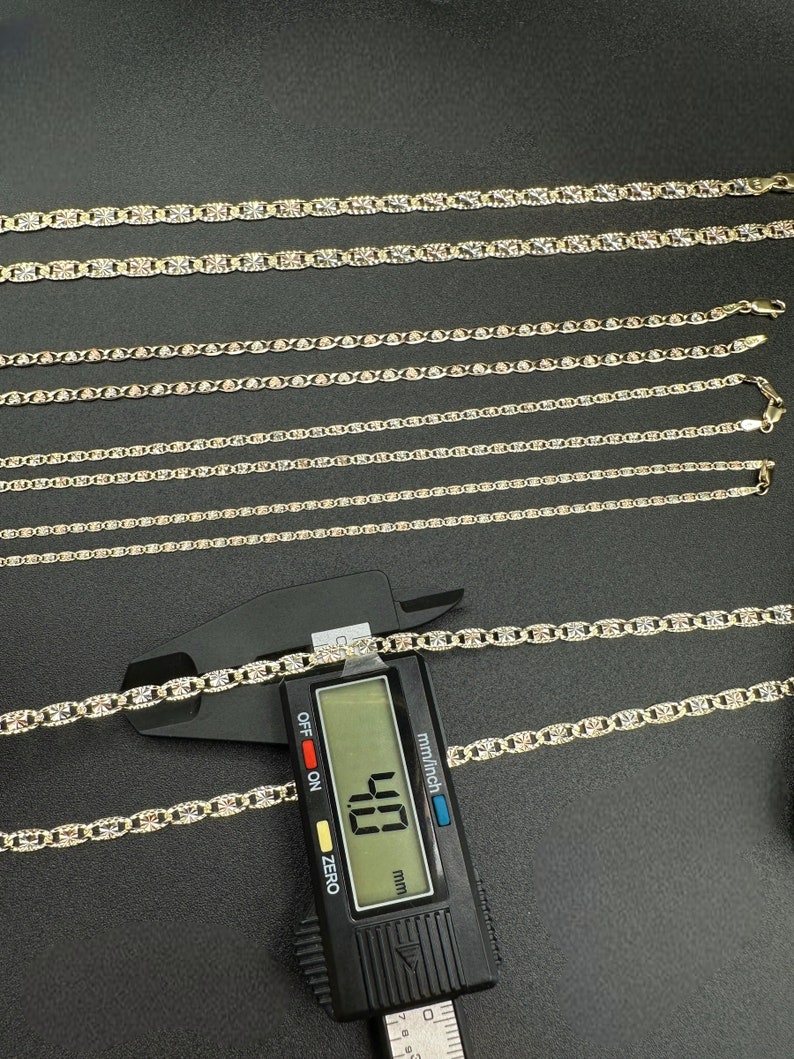 May include: A set of six gold chains of varying lengths, with a digital caliper measuring one of the chains at 4.8 mm. The chains are on a black surface.