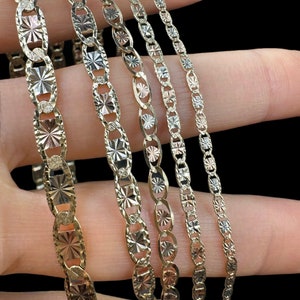 May include: Five gold chains with a diamond-cut pattern. The chains are arranged in a fan shape, with the largest chain at the bottom and the smallest chain at the top.