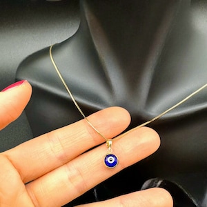 Puede incluir: Un collar de cadena de oro con un colgante de ojo turco azul. El colgante es redondo y tiene un centro blanco.