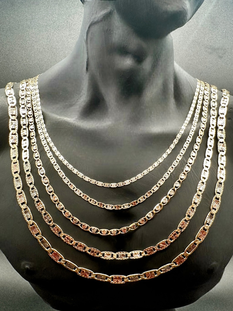May include: A set of six gold chains with a mariner link design. The chains are layered on a mannequin's neck and vary in width.
