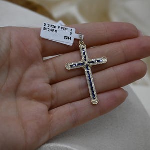Puede incluir: Un colgante de cruz de oro con acentos de zafiro azul y diamantes. El colgante es de 0,82 ct F VVS1 y 0,90 ct. El colgante est&aacute; sobre un fondo blanco.