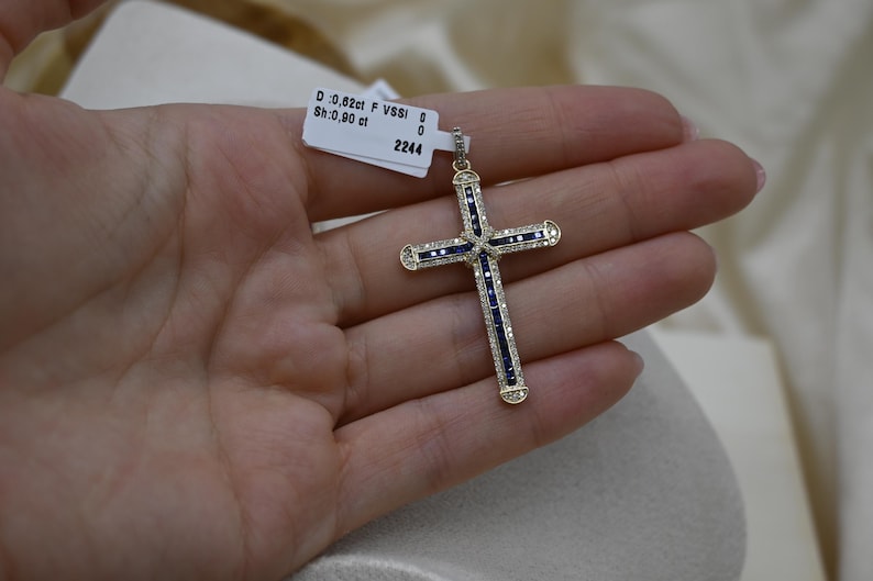 Puede incluir: Un colgante de cruz de oro con acentos de zafiro azul y diamantes. El colgante es de 0,82 ct F VVS1 y 0,90 ct. El colgante est&aacute; sobre un fondo blanco.