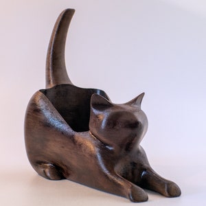 May include: A dark brown wooden cat figurine with a curled tail, designed as a decorative holder or organizer.