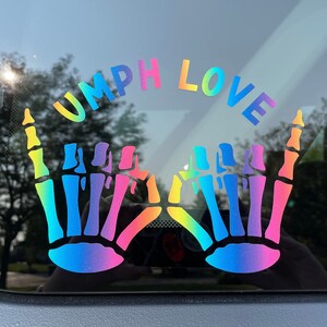 May include: A rainbow-colored skeleton hand sticker with the text "UMPH LOVE" on a car window.