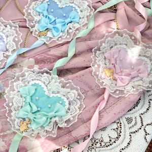 Może przedstawiać: Zestaw trzech serduszek z tkaniny z koronkową lam&oacute;wką. Serduszka są w odcieniach niebieskiego i r&oacute;żowego, z delikatnymi kokardkami i złotymi akcentami.