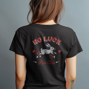 May include: Black t-shirt with a white rabbit running with red accents and the text "No Luck Run Club" printed on the back.