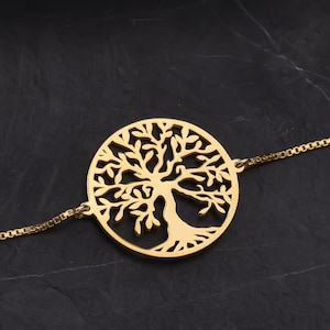 Puede incluir: Un brazalete de cadena dorado con un colgante circular que presenta un diseño detallado de árbol de la vida.