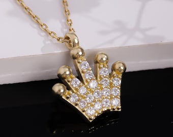 May include: A gold chain necklace with a small, sparkling crown pendant. The crown is adorned with clear cubic zirconia stones.