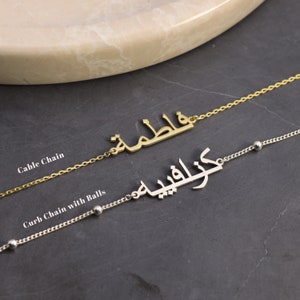 Può includere: Due collane d'oro con scrittura araba. La collana superiore ha una catena a cavo e la collana inferiore ha una catena a curb con piccole sfere.