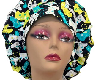 May include: A black, white, yellow, and teal gaming controller patterned bouffant scrub cap. The cap is on a mannequin head. The text "VERNA Made it!" is at the bottom of the image.