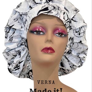 May include: White and black patterned bonnet with a ruffled edge. The bonnet features a repeating design of illustrations. The text "VERNA Made it!" is printed below the bonnet.