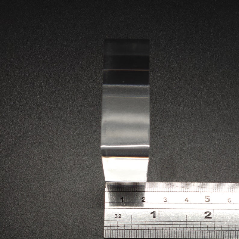 Puede incluir: Una pieza de pl&aacute;stico transparente rectangular, de aproximadamente 5 cm de largo, se mide con una regla. La regla est&aacute; marcada en cent&iacute;metros y mil&iacute;metros.