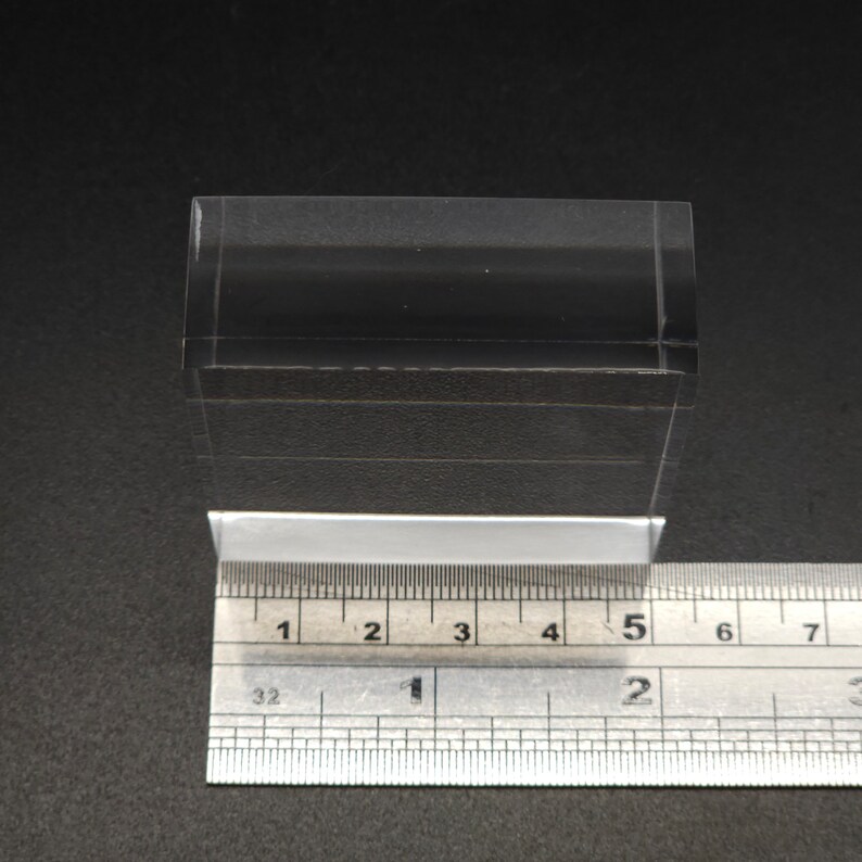 Puede incluir: Un bloque de acr&iacute;lico transparente que mide 12,7 cm de largo. El bloque est&aacute; sobre una regla para la escala.