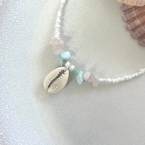 May include: A white beaded necklace with a shell pendant and pink and blue gemstone accents.