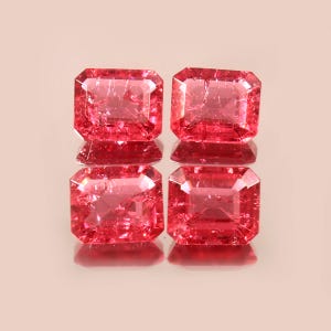 May include: Four pink gemstones with a rectangular emerald cut. The gemstones are displayed on a reflective surface.