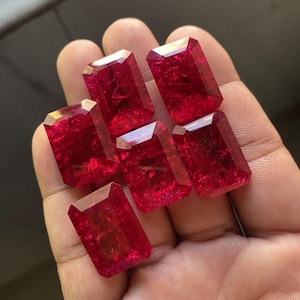 以下が含まれることがあります： 深紅色のエメラルドカットの宝石が7つ。宝石はファセットカットされており、高い光沢があります。