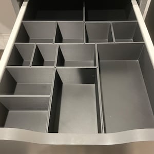 May include: A gray drawer organizer with multiple compartments of varying sizes. The organizer is made of a textured plastic material.
